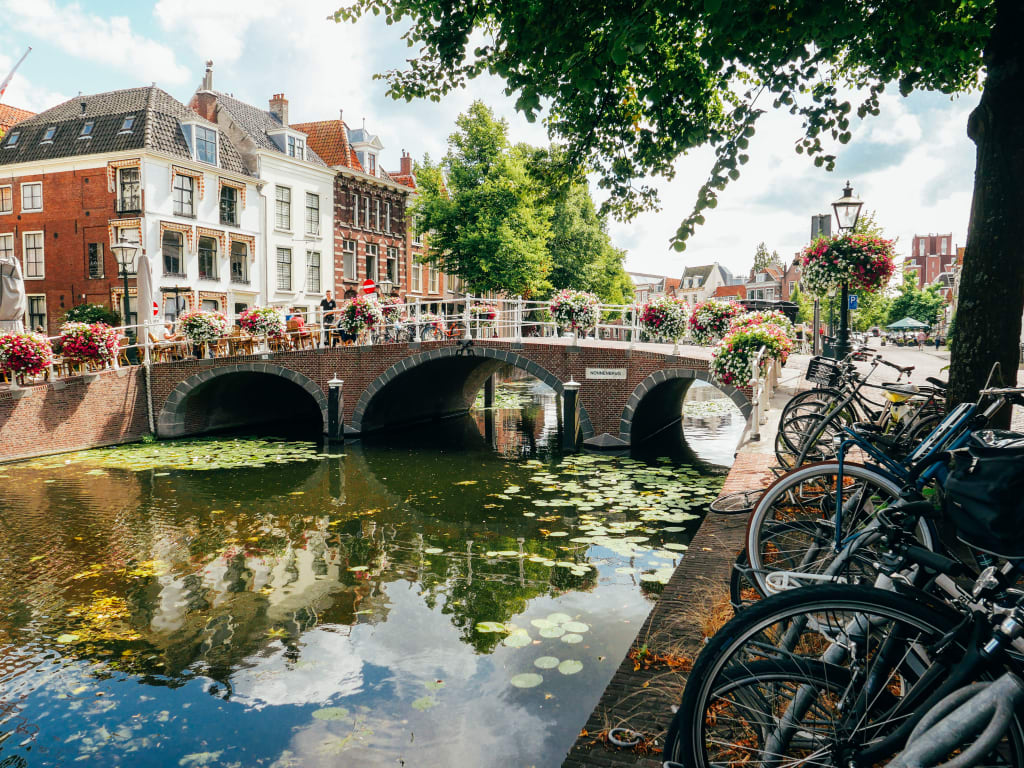 Biciclette parcheggiate su un ponte con canale e case storiche, Amsterdam, Olanda